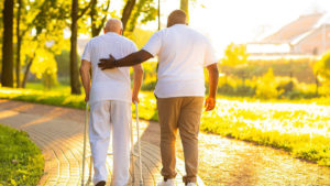 Senior Living Worker Retention - male aid helps senior man walk with his walker