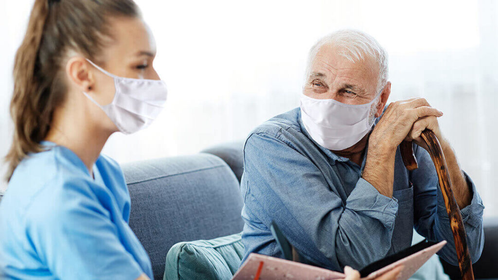 Senior man in mask smiling at nurse wearing a mask